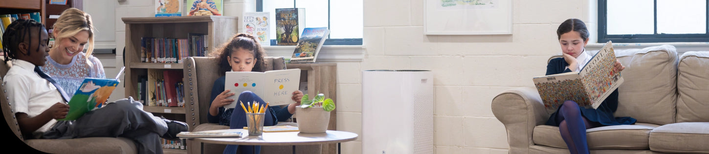 a student reading a book on a couch in the library next to an air purifier
