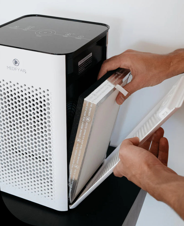 a person changing the air filter in a air purifier on top of a table.