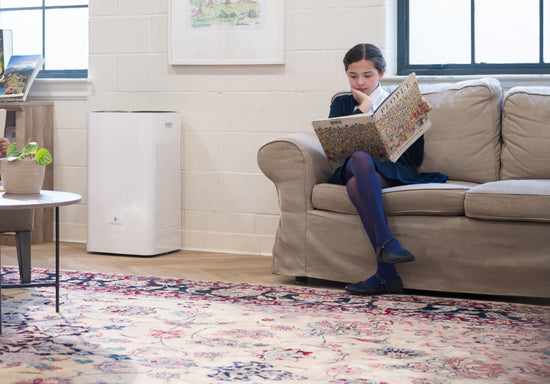 a student reading a book on a couch in the library next to an air purifier