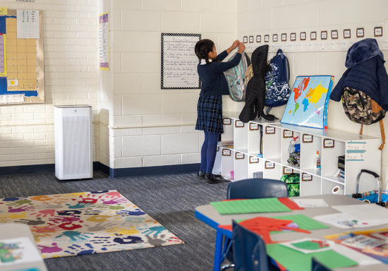 kid putting away a backpack in a classroom next to an air purifier.