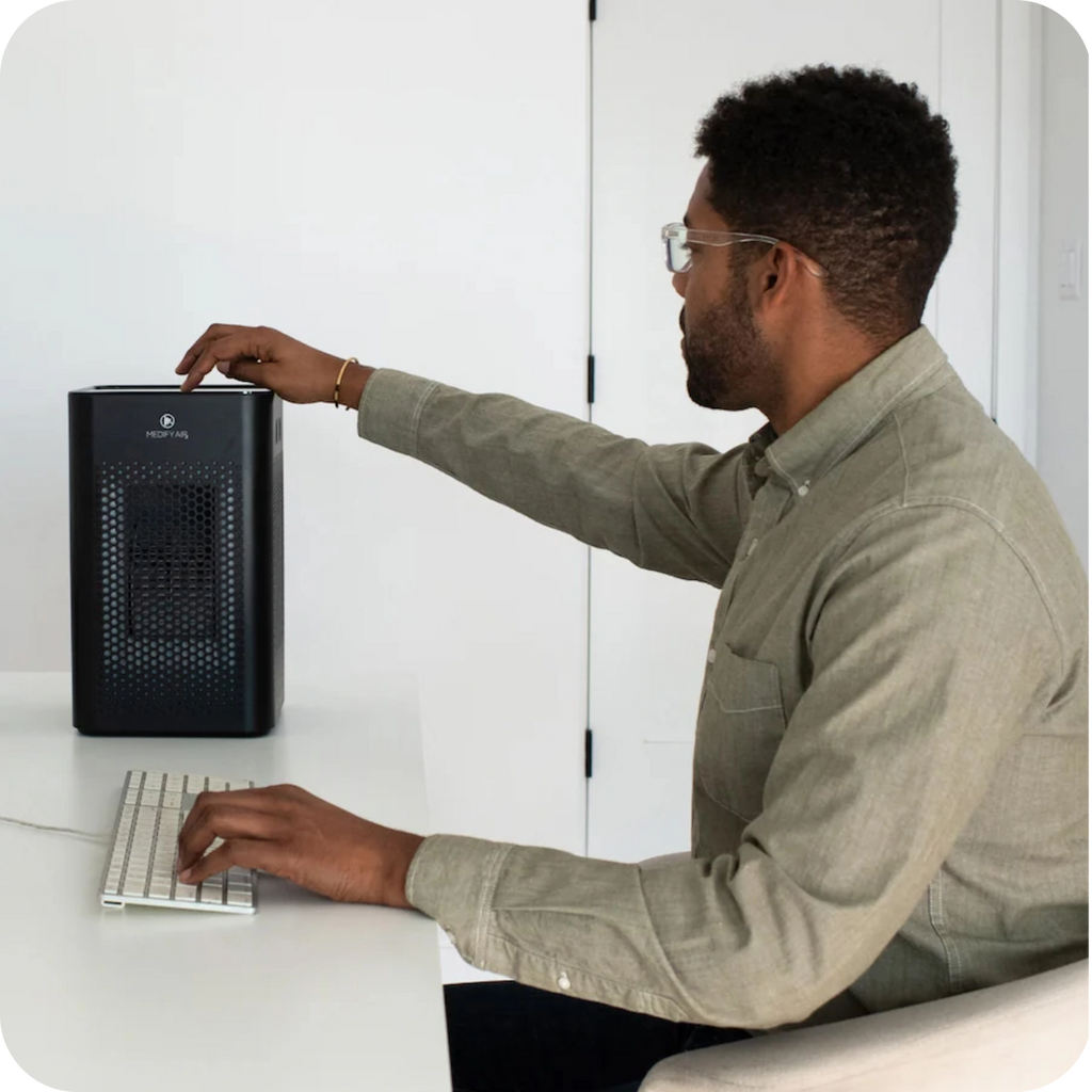 a person sitting at their office desk turning on their desktop air purifier